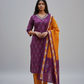 Woman in a purple and orange traditional outfit standing in front of a stone building with flowers.